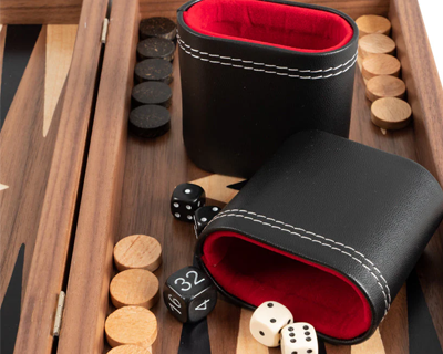 Wooden backgammon board with checkers, dice, and black dice cups with red interior.